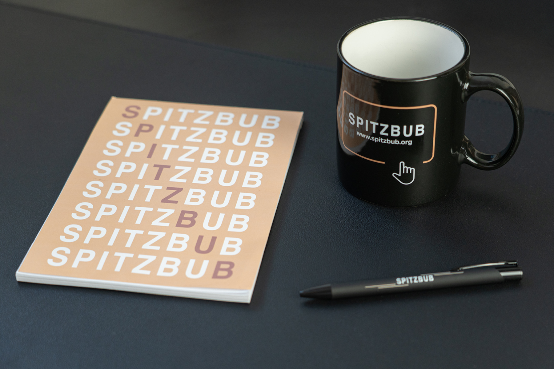 Notizbuch, Stift und Tasse von Spitzbub liegen auf einem Tisch